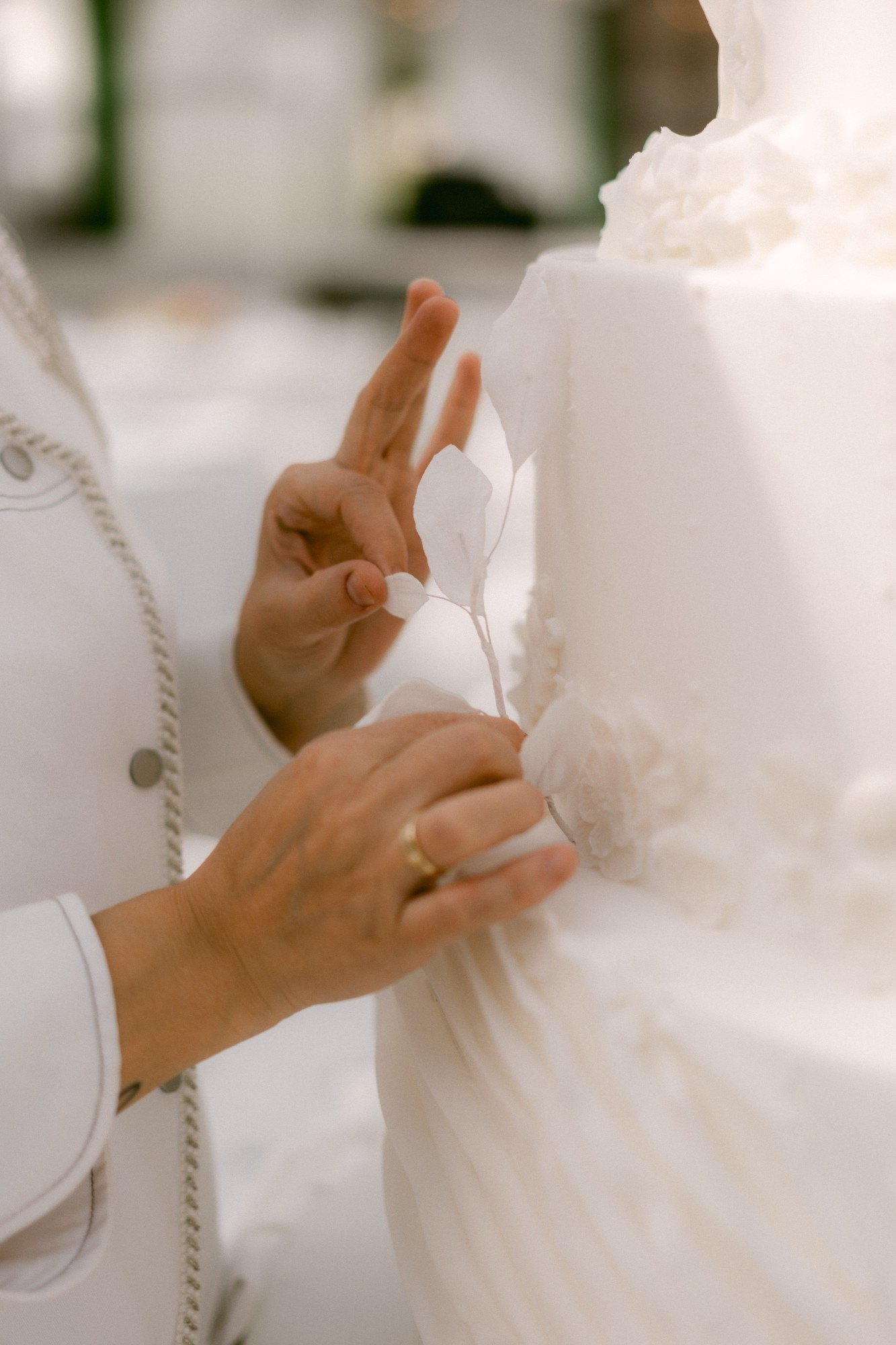 Nelly's hands placing a delicate hand-made sugar leaf spray onto a white wedding cake